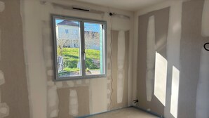 Ein Zimmer mit freiliegenden Wänden, einem großen Fenster und einer blauen Fußleiste.