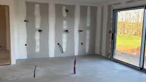 Ein Zimmer mit freiliegenden Wänden, einem Betonboden und einer großen Glasdoor, die nach draußen führt.