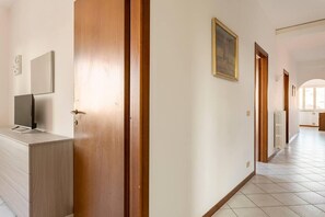 A hallway with wooden doors, a tiled floor, and a television on a cabinet. - Three Bedroom Apartment (Montecatini Terme)