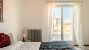 Un dormitorio con cama, radiador y ventana con cortinas.
