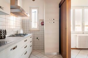 Uma cozinha moderna com azulejos brancos, fogão a gás, coifa e janela.
