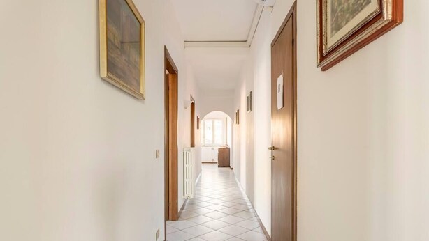 Un pasillo con piso de baldosas, puertas de madera y cuadros en las paredes.