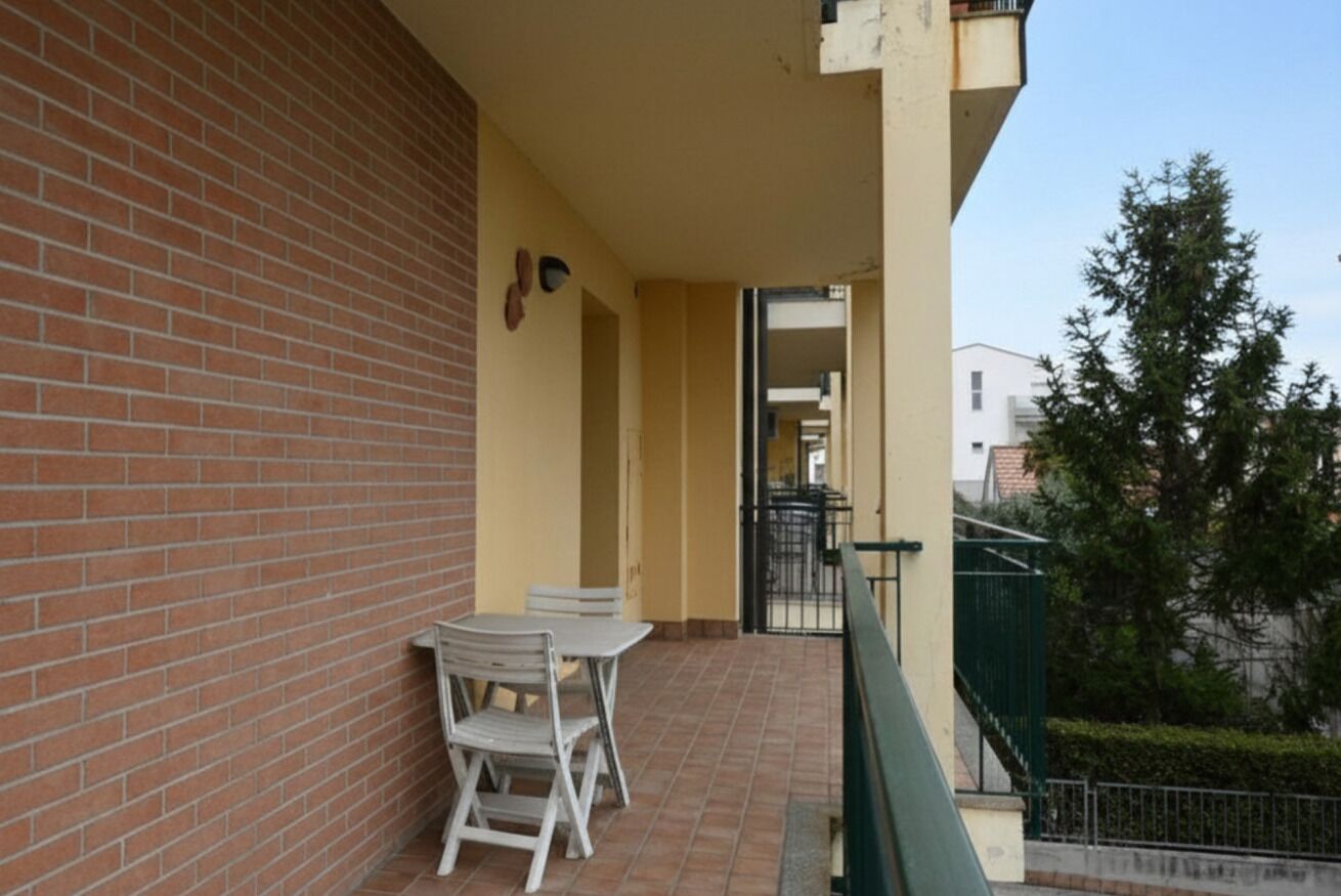 A balcony with a brick wall, a table with chairs, and a view of the street.