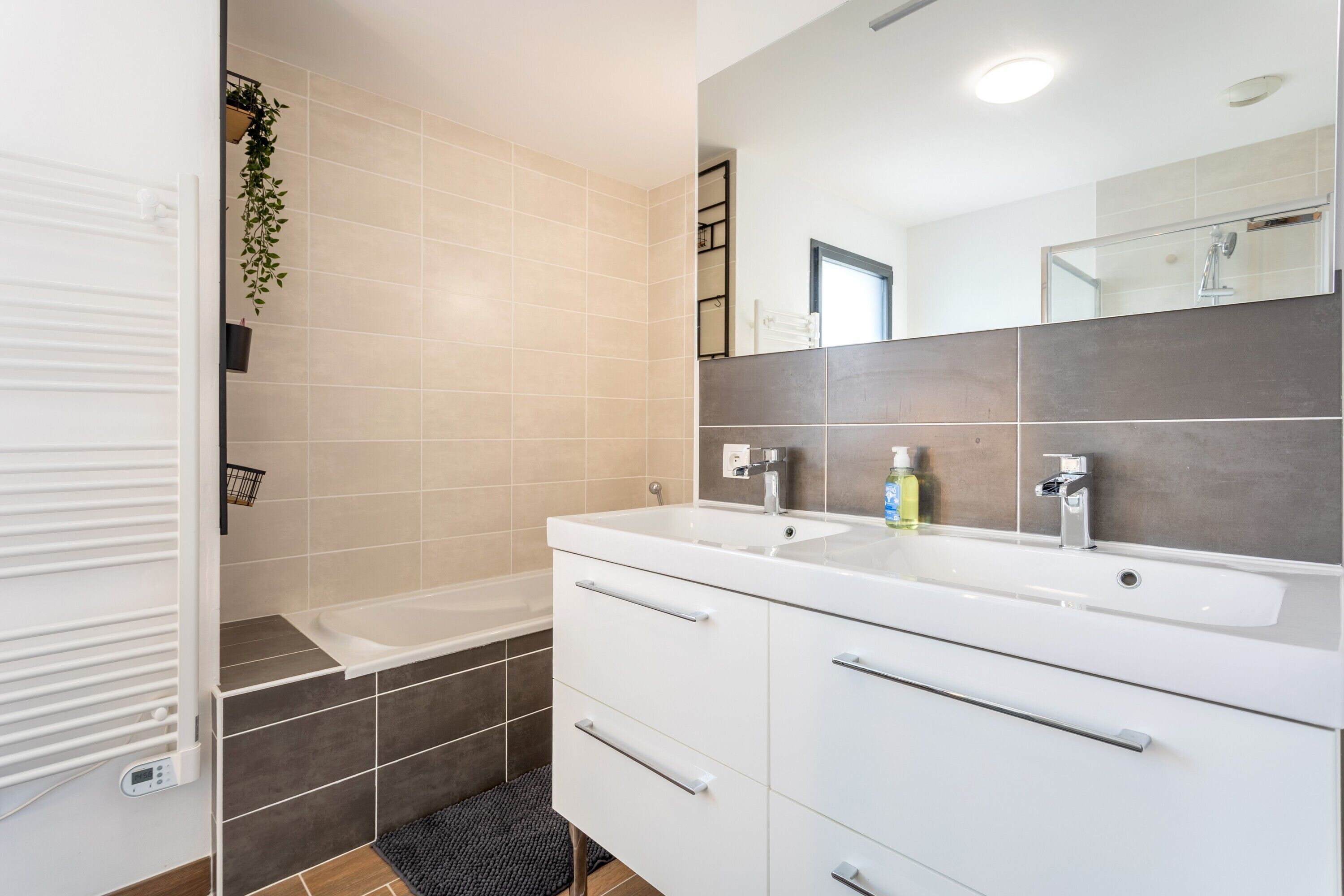 A modern bathroom with a double sink, a bathtub, and a large mirror.