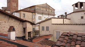Um edifício histórico com uma torre de sino, um pátio com telhados de telha vermelha e uma mistura de estilos arquitetônicos.