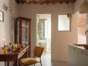 Eine Küche mit einem Holzkasten, einem Stuhl, einem Esstisch mit Frühstücksgebäck und einem Fenster mit einer Pflanze.