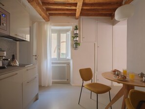 Eine Küche mit Kaffeemaschine, Wasserkocher und Heizkörper. Ein Essbereich mit Tisch, Stühlen und Frühstücksgebäck.