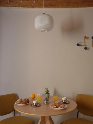 A round wooden table with breakfast items, two chairs, a hanging light fixture, and a wall decoration. - One Bedroom Apartment (Lucca)