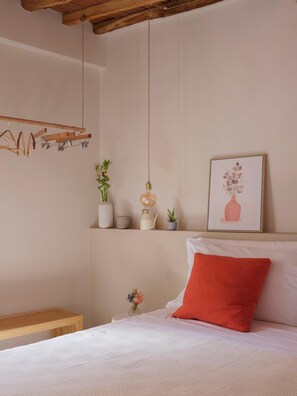 Ein Schlafzimmer mit einem Bett, einer Hängeleuchte, einem gerahmten Bild und einem Holzregal mit Pflanzen.