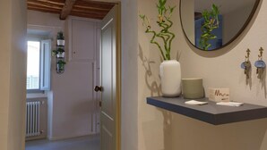 A hallway with a door leading to a room, a radiator, and a wall-mounted mirror reflecting a plant.