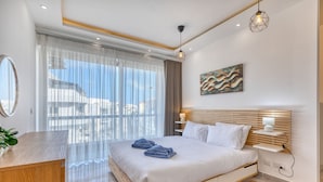 A modern hotel room with a large bed, a wooden desk, a bedside table, a wall-mounted lamp, and a view of the sea. - Luxury duplex apartment, sun terrace, jacuzzi SDIN1-1 (Swieqi)