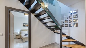 A modern staircase with glass railings and wooden steps, leading to a bedroom with a bed and bedside table. - Luxury duplex apartment, sun terrace, jacuzzi SDIN1-1 (Swieqi)