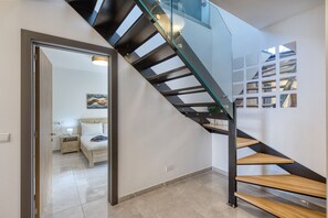 A modern staircase with glass railings and wooden steps, leading to a bedroom with a bed and bedside table. - Luxury duplex apartment, sun terrace, jacuzzi SDIN1-1 (Swieqi)