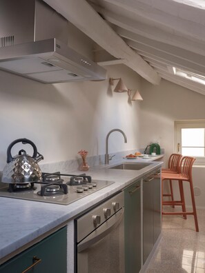 A kitchen with a gas stove, kettle, and a window with a view. - One Bedroom Apartment (Lucca)