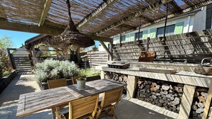 An outdoor patio with a wooden table and chairs, a thatched roof, and a stone wall with stacked logs. - Charming gîte near the Côte Viticole (Chevigny-en-Valière)