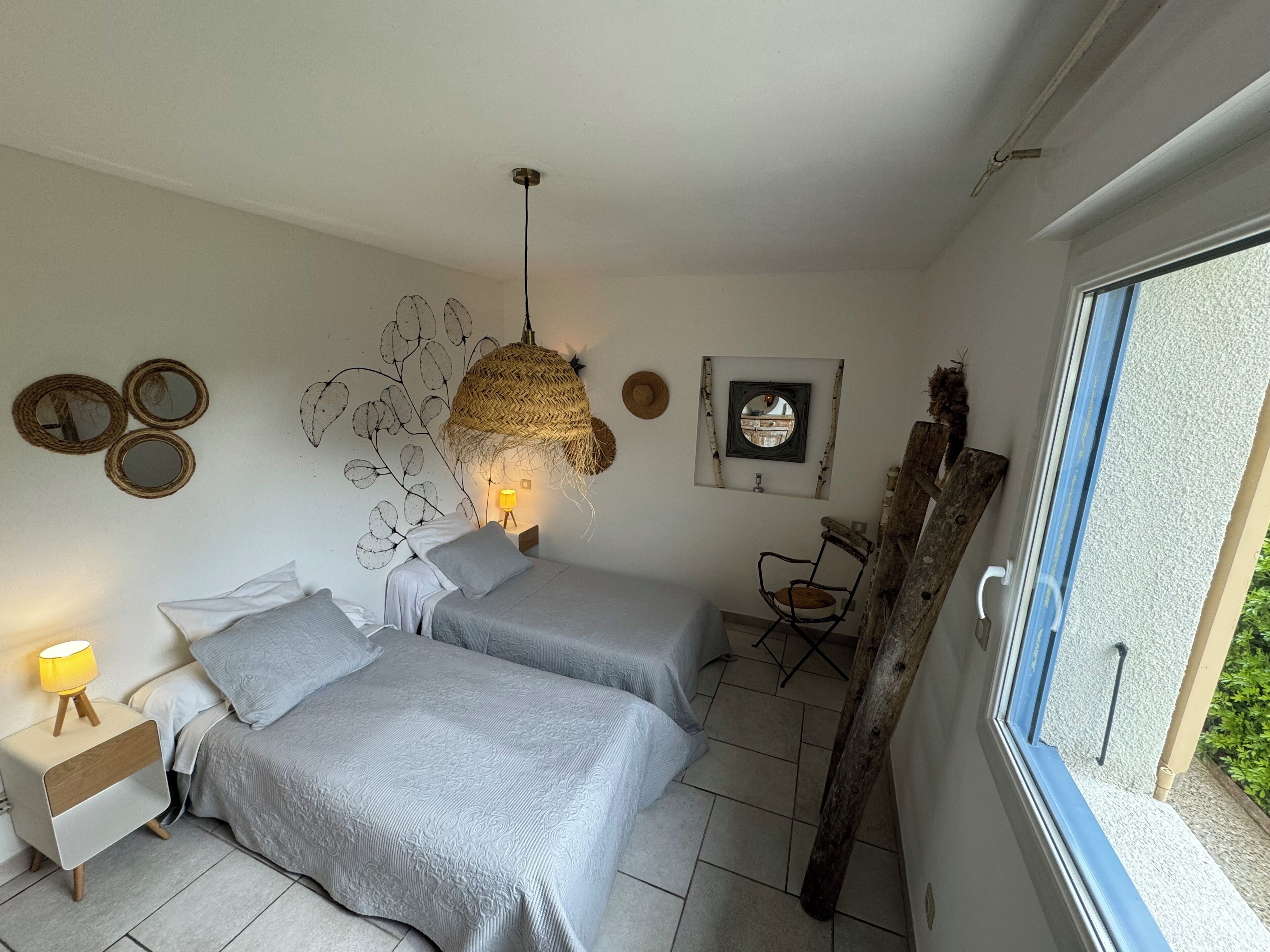 Un dormitorio con dos camas, un lámpara colgante, decoración en la pared y una ventana con vistas.