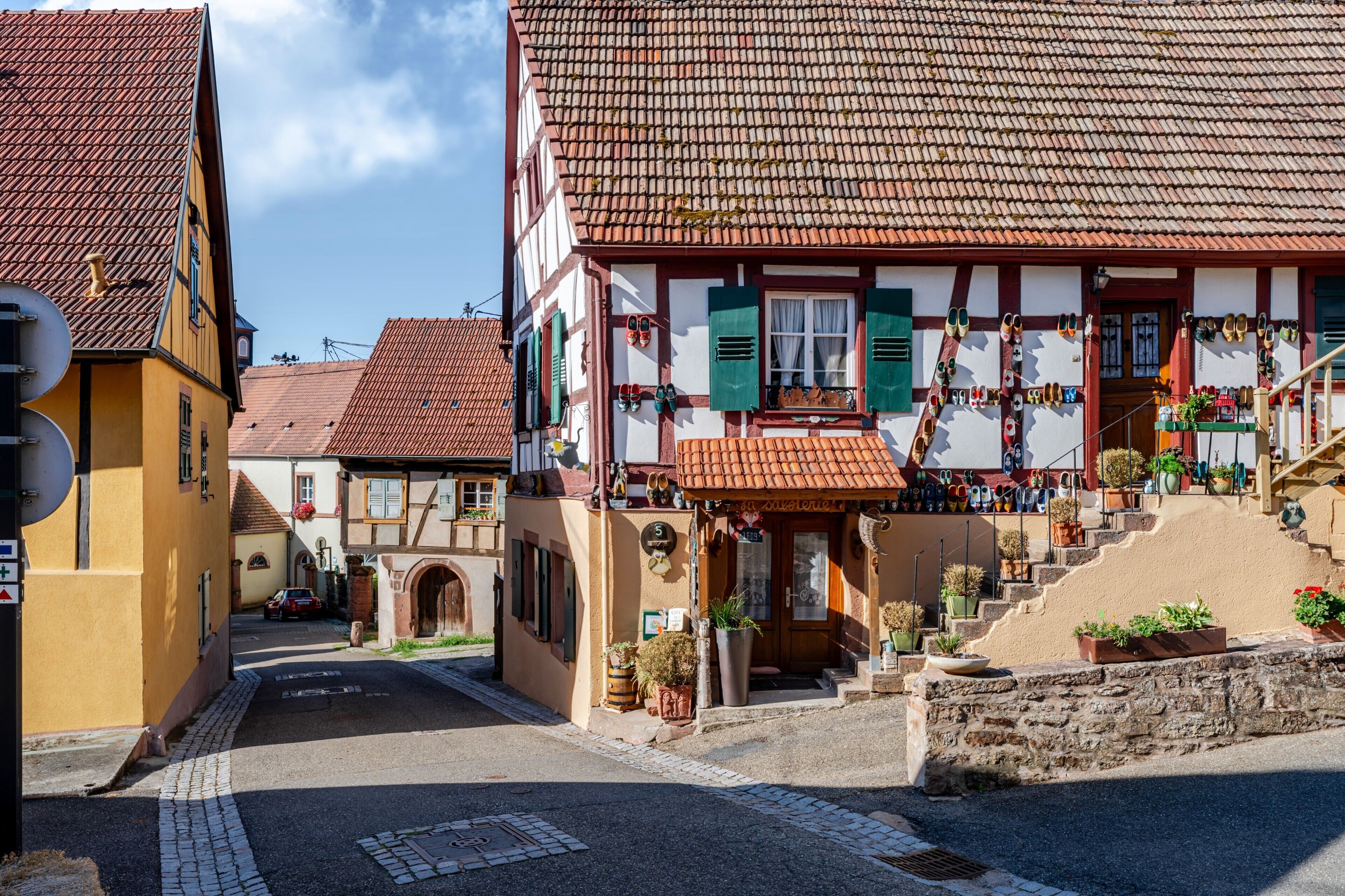 Een typische Europese straat met een rij vakwerkhuizen, een geplaveid voetpad en een kleine trap naar een winkel met schoenen die buiten staan.