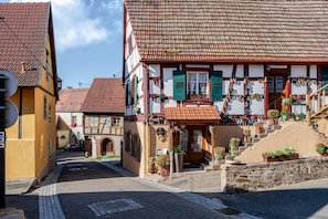A traditional European street with a row of half-timbered houses, a cobblestone street, and a small staircase leading to a shop with shoes displayed outside.
