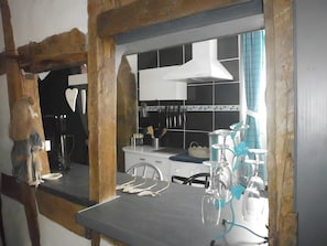 A kitchen with a white countertop, hanging utensils, and a blue curtain. - Gite "La Saboterie 1609" in Oberbronn (Oberbronn)