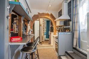 A narrow kitchen with a stone archway, a bar area with stools, and a view into a bedroom.