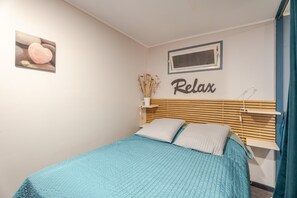 A bedroom with a bed, a wall-mounted shelf with a vase, and a framed picture.