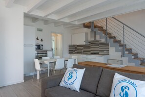 Eine moderne Küche mit weißen Schränken, ein Essbereich mit weißen Stühlen und eine Treppe mit Holzboden.