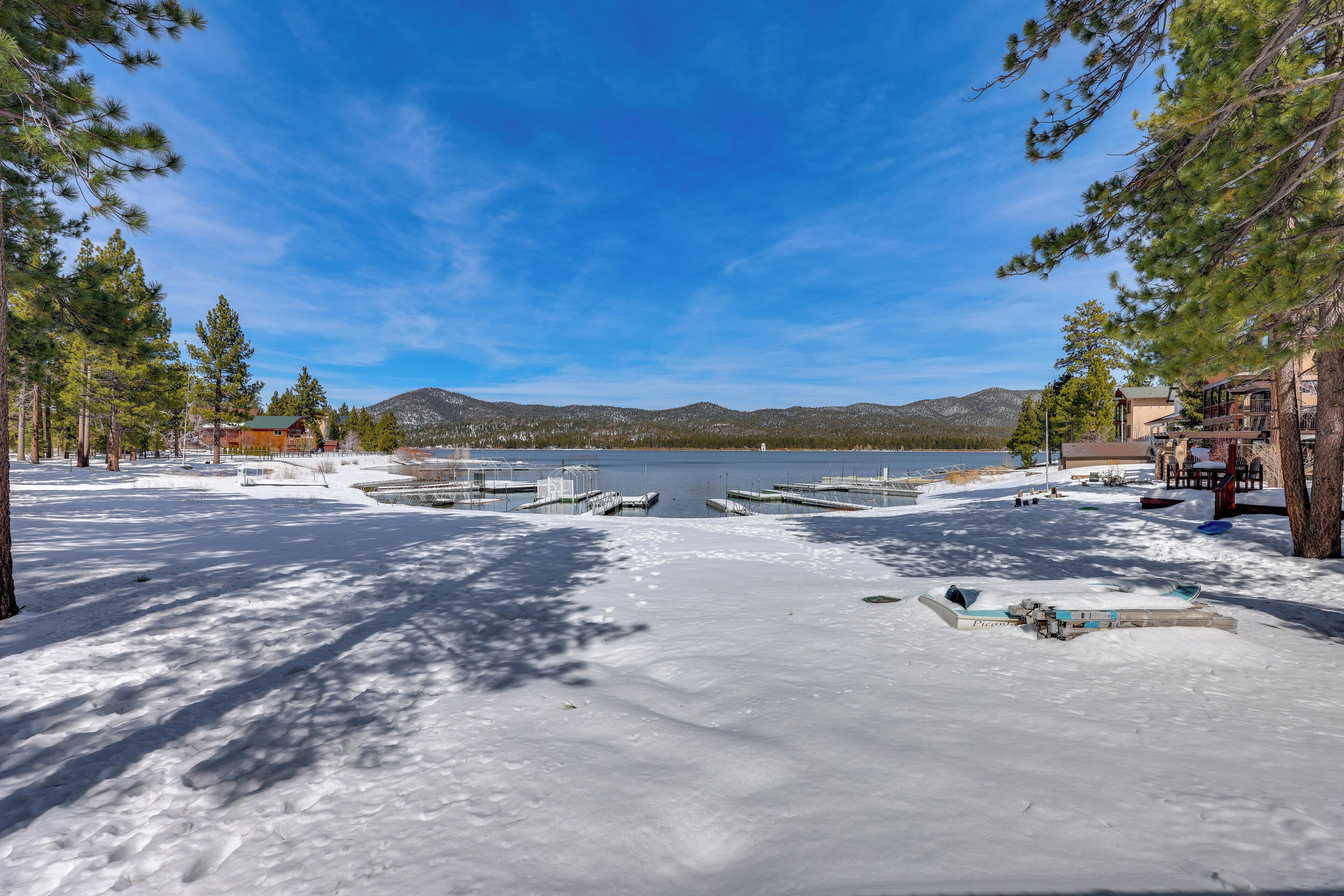 A snow-covered lake with docks, surrounded by pine trees and buildings.
