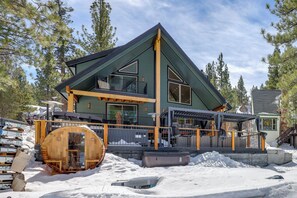 Ein modernes Chalet mit einer großen Terrasse, einer Sauna und verschneitem Gelände.