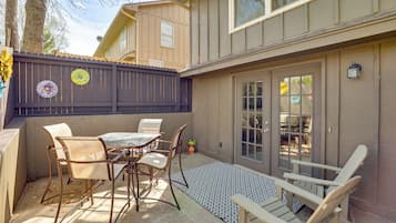 A patio with a table and chairs, a wooden fence, and a building with a window and door.