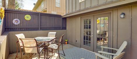 A patio with a table and chairs, a wooden fence, and a building with a window and door.