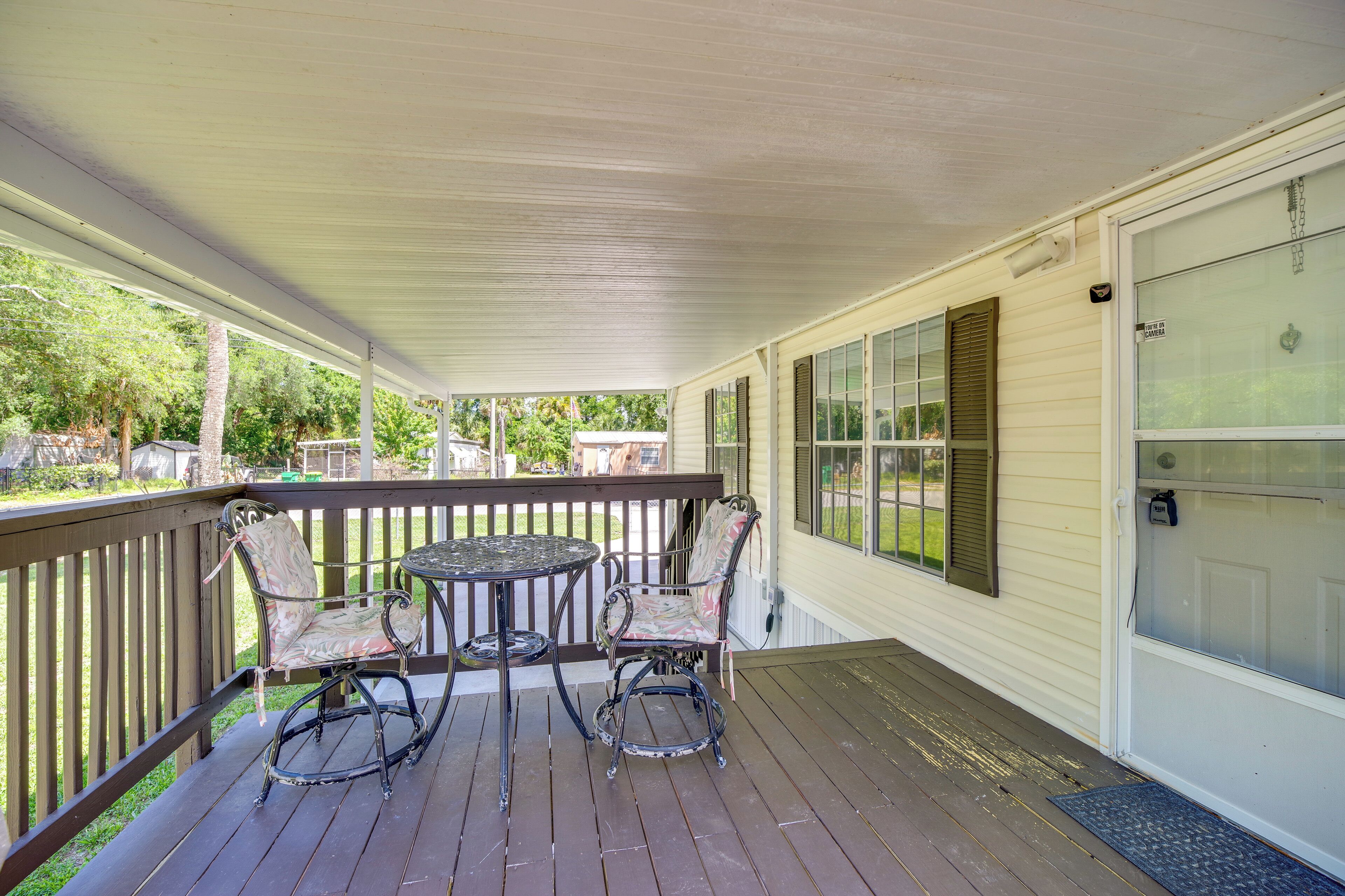 A covered porch with a table and chairs, a door with a window, and a view of the outdoors.