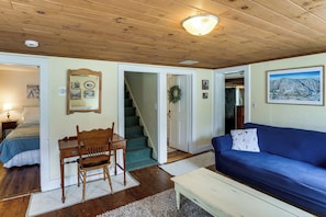 A room with a wooden ceiling, a blue sofa, a wooden chair, a desk, and a staircase leading to another room.