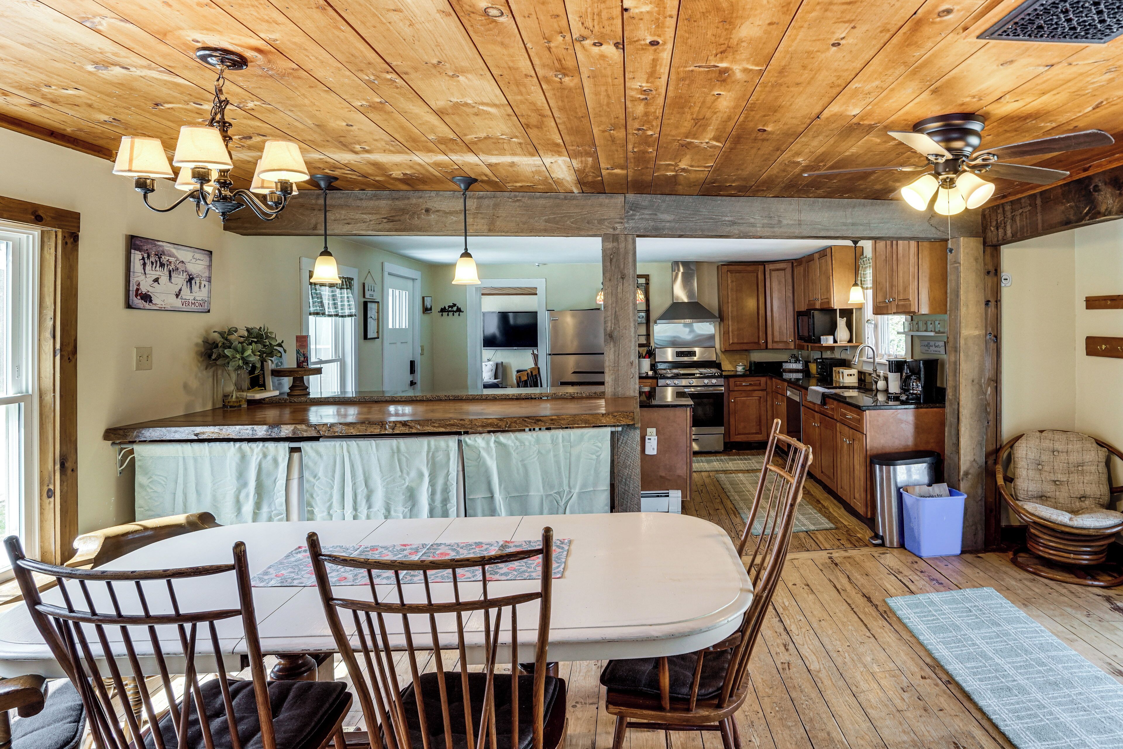 A wooden ceiling, a dining table with chairs, a kitchen area with appliances, and a chair.
