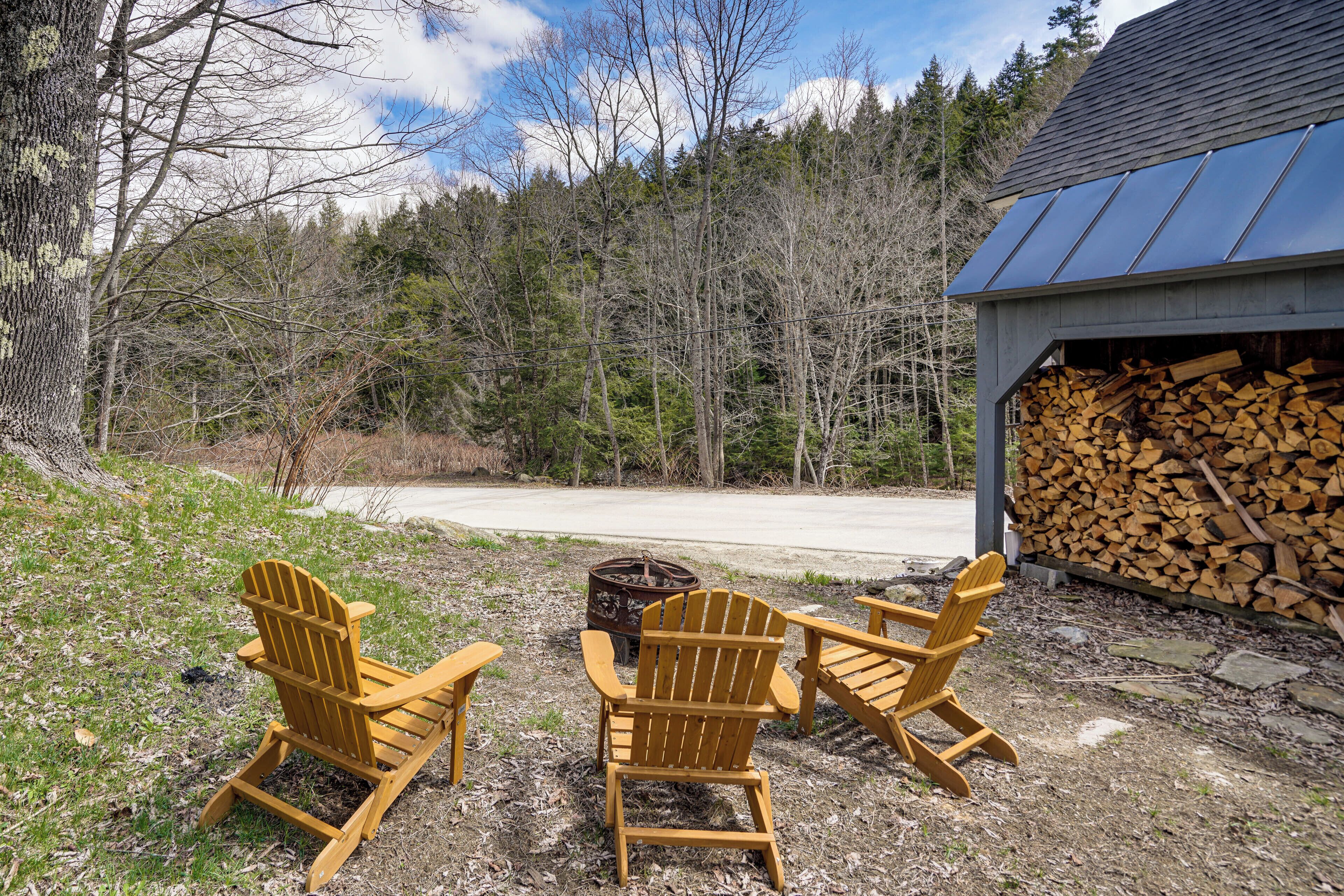 A wooden deck with Adirondack chairs, a fire pit, and a stack of firewood.