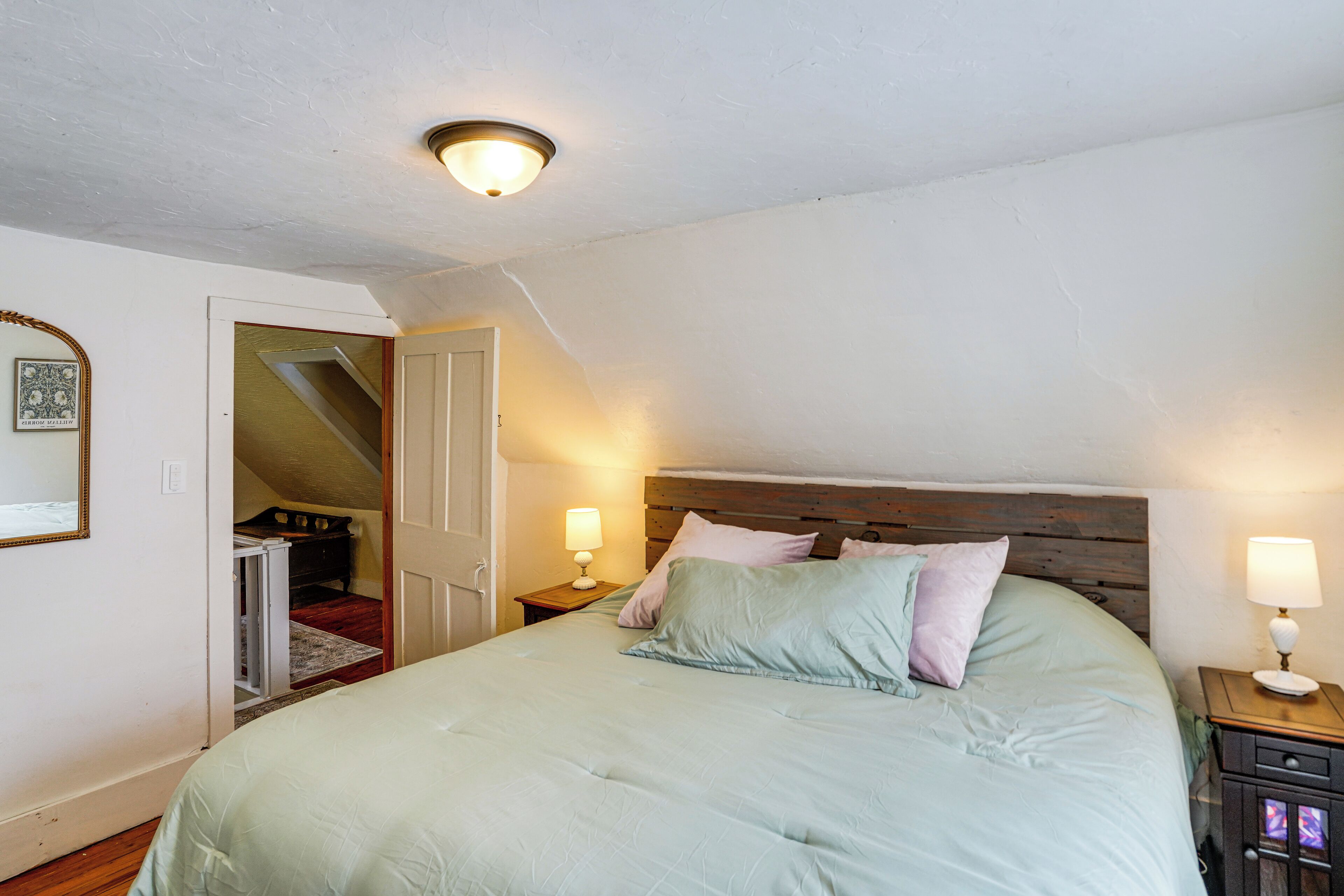 Quarto com uma cama grande, duas luminárias de cabeceira, um painel de madeira na cabeceira e uma porta que dá para outro cômodo.