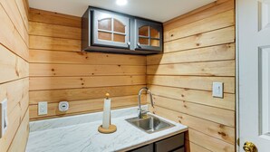 Una cocina compacta con paredes de madera, una encimera de mármol, un lavabo y un pequeño armario sobre el lavabo.