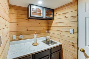 A compact kitchen with wooden walls, a marble countertop, a sink, and a small cabinet above the sink.