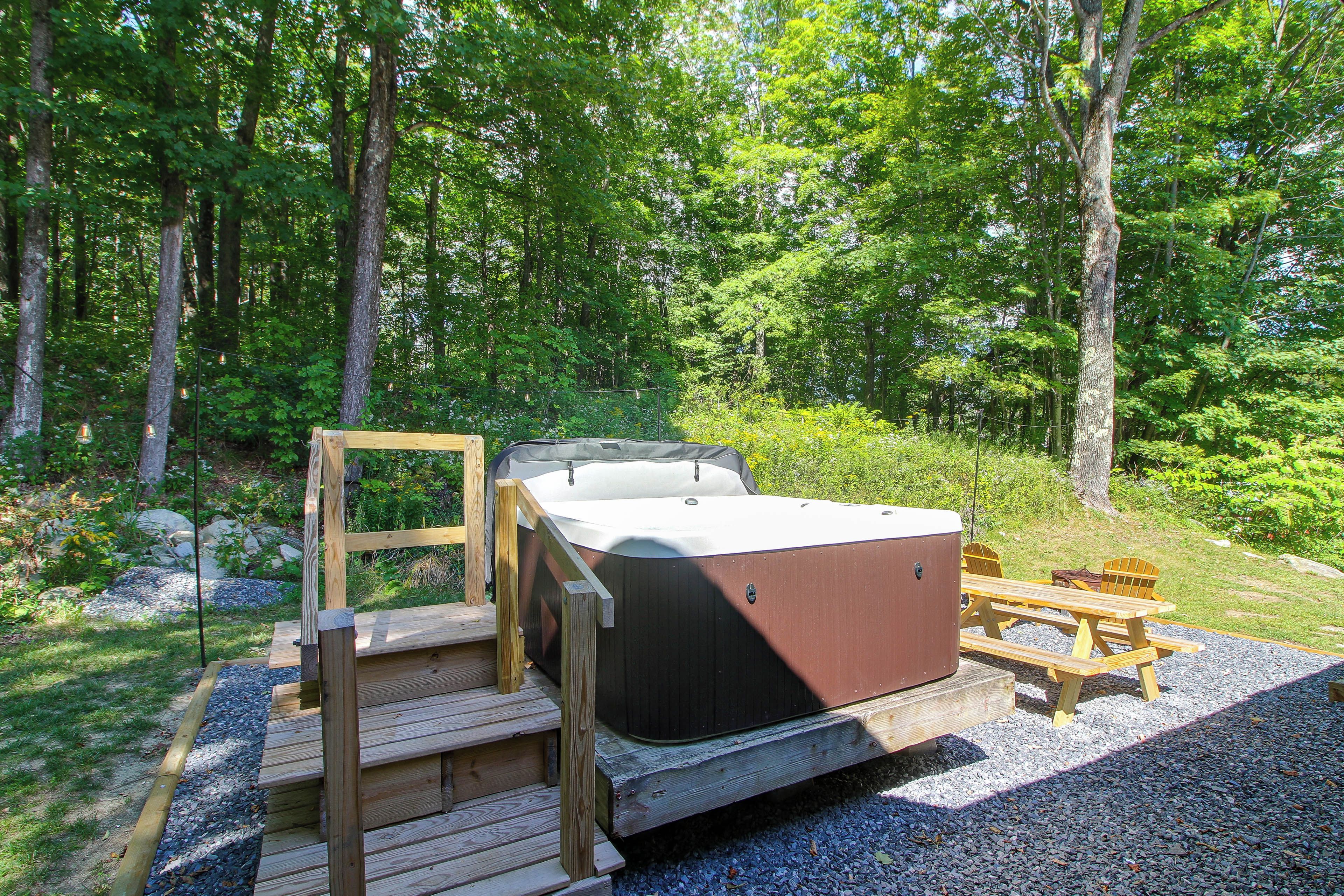 Ein Whirlpool mit einer Holzterrasse und Treppen, umgeben von bewaldetem Gelände.
