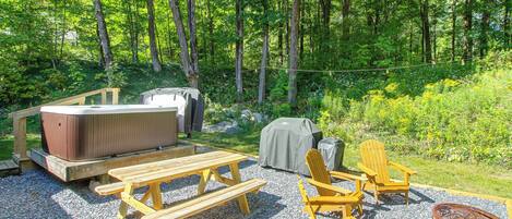 A wooden deck with picnic tables, Adirondack chairs, a hot tub, and a fire pit.