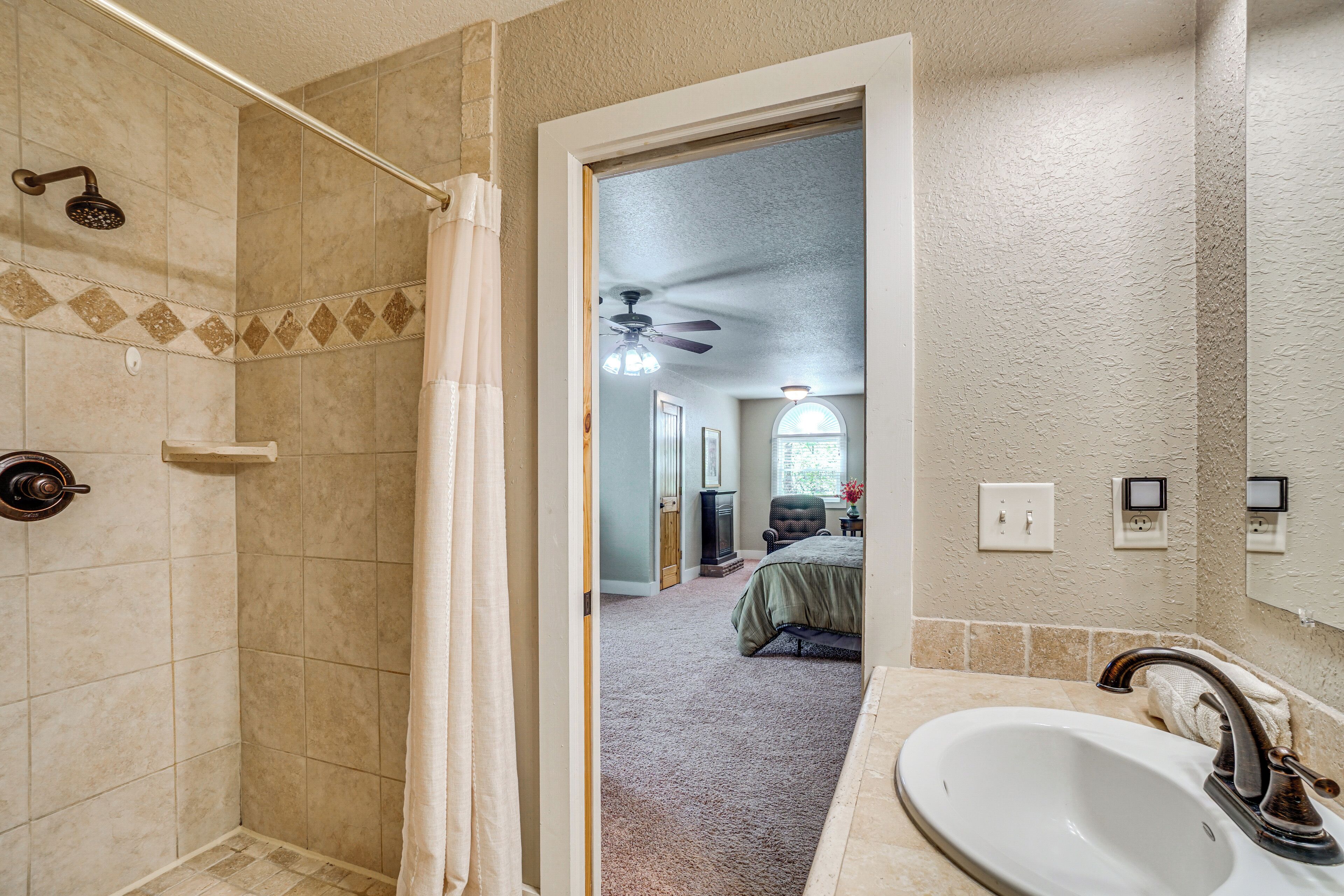 A bathroom with a shower, a sink, and a doorway leading to a bedroom.