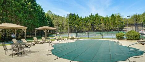 An outdoor patio area with a tennis court, lounge chairs, and a gazebo.