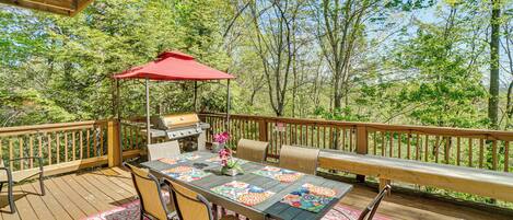 A wooden deck with a table, chairs, a grill, and a red umbrella.