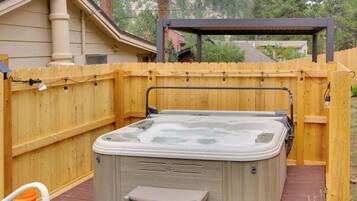 Un jacuzzi en un patio trasero con valla de madera, una pérgola y vista de una casa vecina.