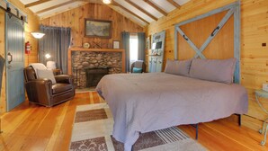Ein gemütliches Schlafzimmer in einer Blockhütte mit einem großen Bett, einem Kamin, einem Ledersessel und Holzwänden.