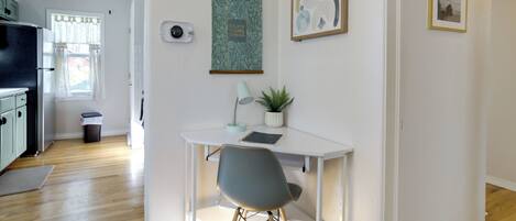 Una cocina moderna con suelo de madera, una mesa de comedor blanca con una silla gris, una lámpara en el techo y una planta colgante en la pared.