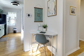 Une cuisine moderne avec un plancher en bois, une table à manger blanche avec une chaise grise, un luminaire au plafond et une plante fixée au mur.