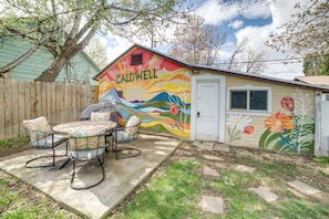 Une maison ornée d’une fresque murale aux couleurs vives, une terrasse avec des chaises et une clôture en bois.