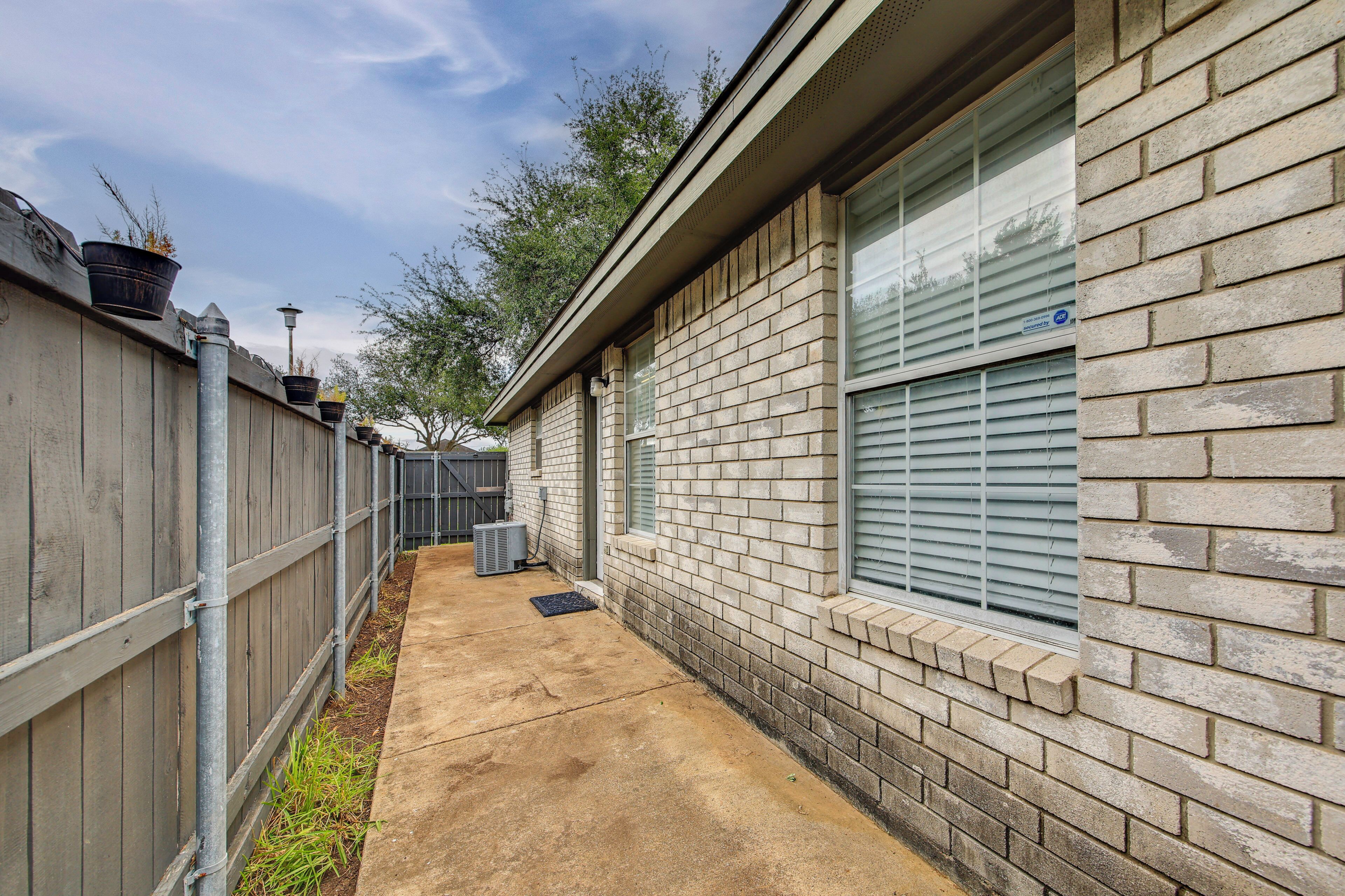 A brick building with a concrete pathway, a wooden fence, and a window with blinds.