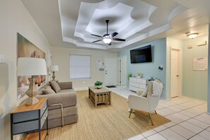 Ein Wohnzimmer mit Deckenventilator, einer Couch, einem Couchtisch und einem an der Wand befestigten Fernseher.