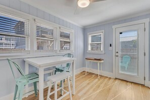 Una habitación con una mesa blanca y sillas, una mesita auxiliar pequeña y una puerta con un panel de vidrio esmerilado.